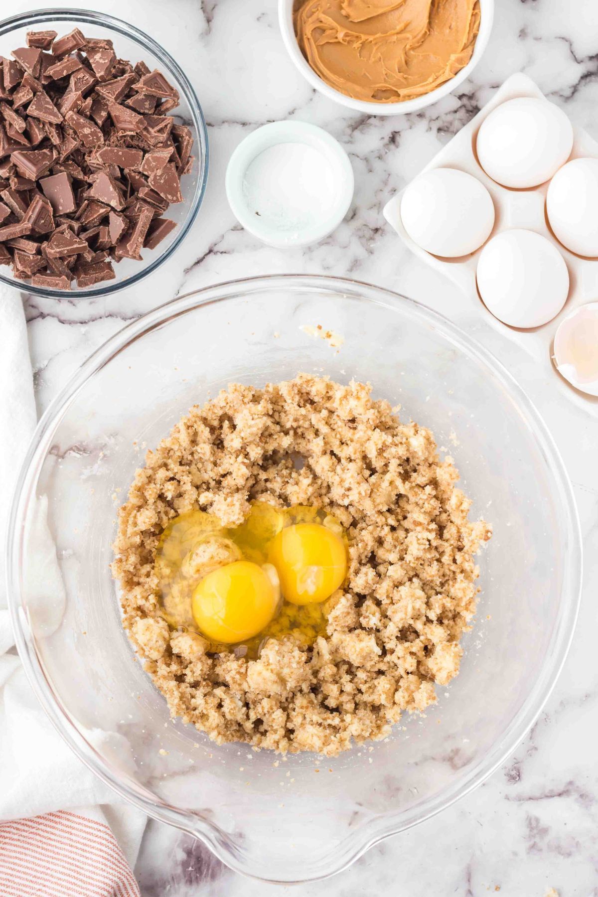 Eggs being added to sugars and butter in a clear mixing bowl. 
