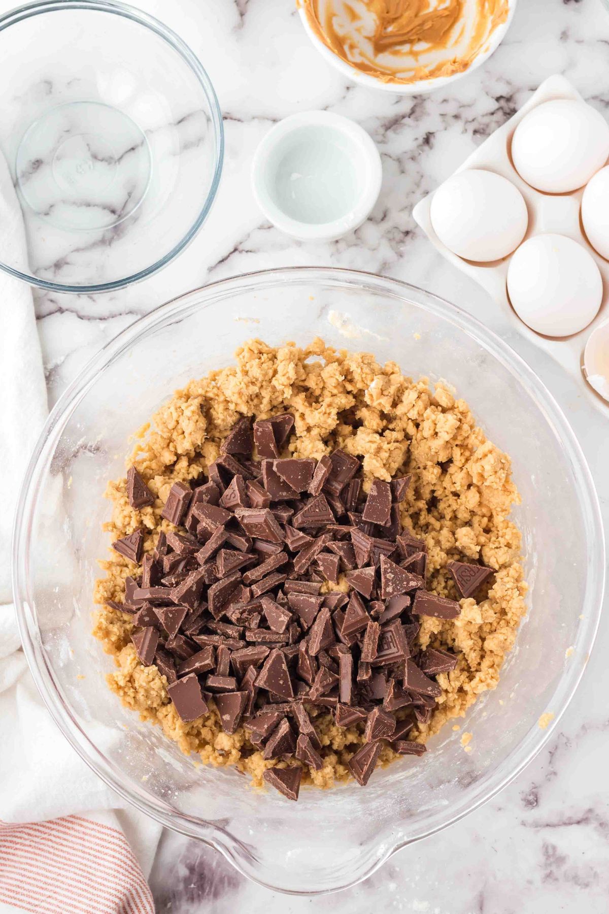 Chocolate chunks being added to cookie dough in a clear glass bowl. 