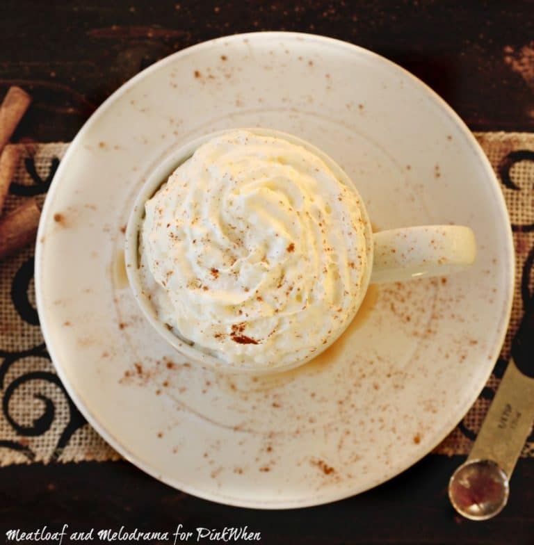 cinnamon-cocoa hot chocolate in a white cup on a white plate with cinnamon sprinkled around.