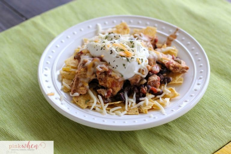 Chicken Crock Pot Tacos on a bed of tortilla chips, smothered in sour cream and cheese on a white plate.