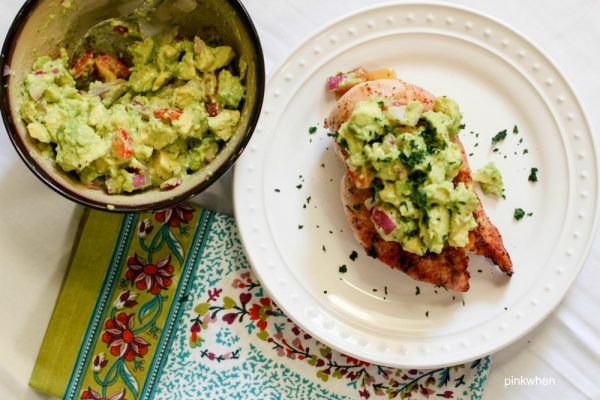 grilled chicken on a white plate with a topping and side bowl of avocado salsa.