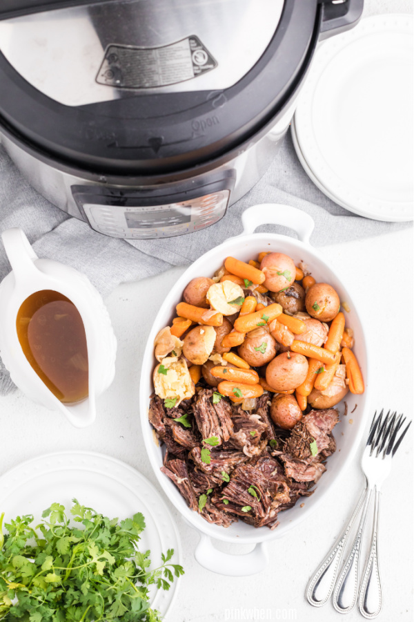 Pot roast made in the pressure cooker and served in a white dish next to a gravy boat.