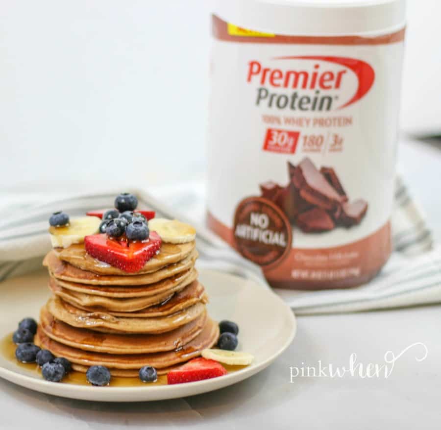 Stacked protein pancakes with fruit on a white plate.