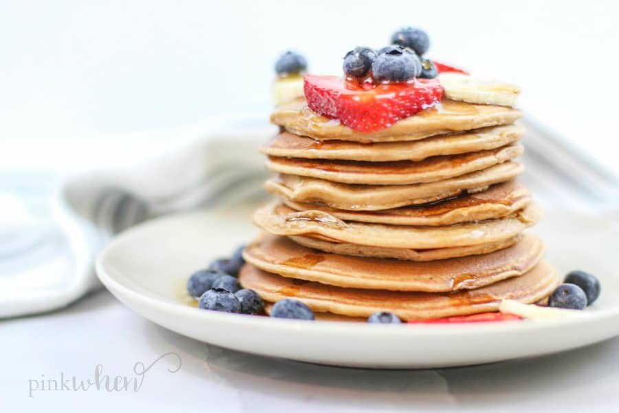 Protein pancakes covered in fruit on a white plate. 