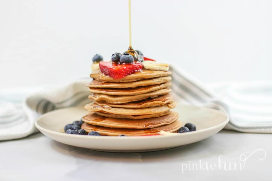 Protein Pancakes with fruit and being drizzled in syrup on a white plate. 