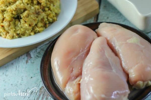 boneless skinless chicken breast on a brown plate with stuffing of a white plate in the background