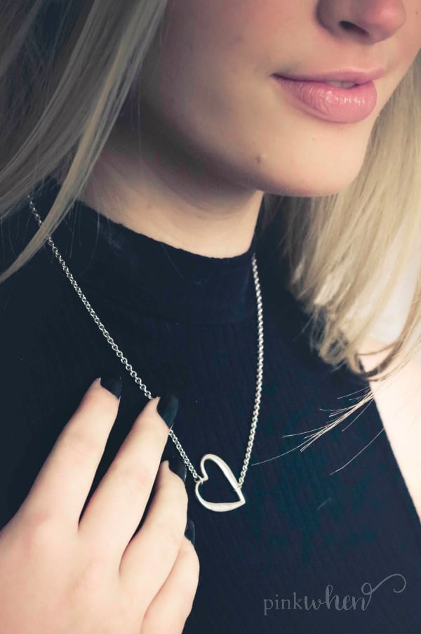 girl in black touching a heart shaped necklace.
