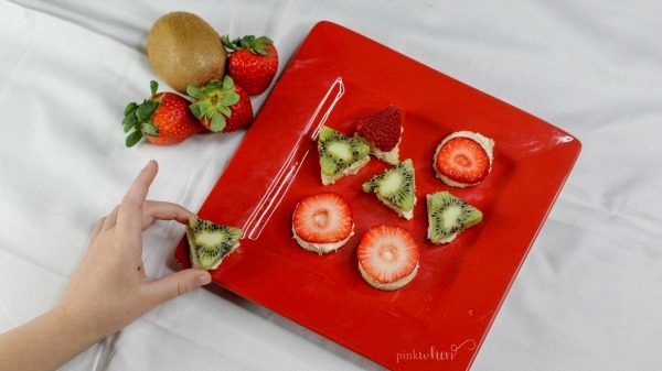 Christmas Sugar Cookies topped with cream cheese frosting and topped with fresh fruit on a red plate. 