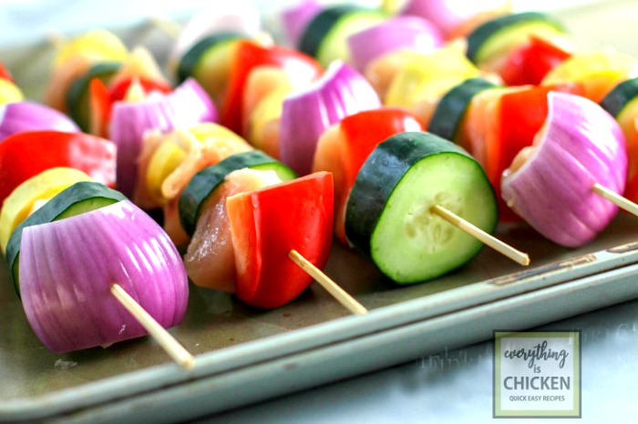 Chicken and vegetables on skewers lined up on a tray. 