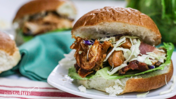 Shredded Slow Cooker BBQ Chicken served on a bun with toppings. 