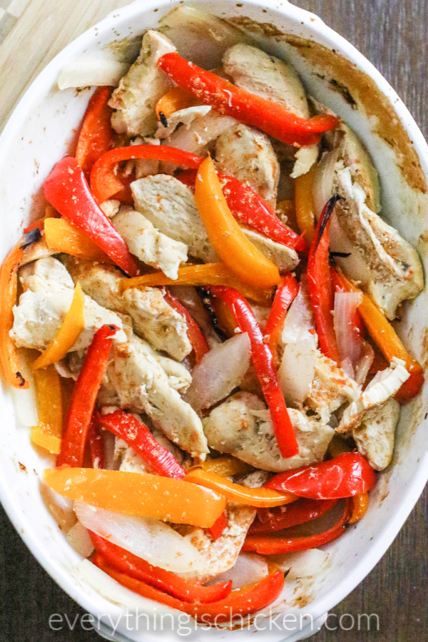 Oven baked chicken fajitas and peppers in a white baking dish.