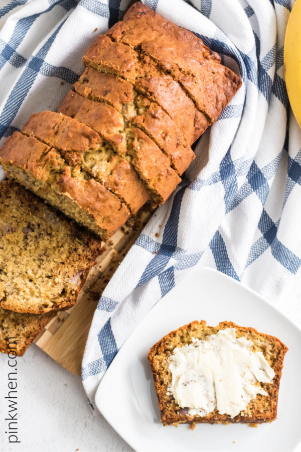 Banana bread sliced and served with a buttered piece of bread on a plate.