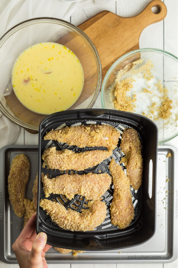 breaded chicken strips in an air fryer basket.
