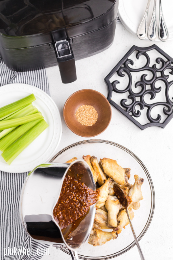 Wing sauce being poured over cooked wings.