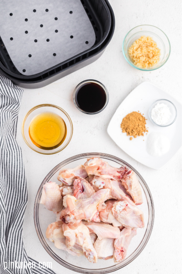 Air Fryer basket and ingredients needed for chicken wings on a white table. 