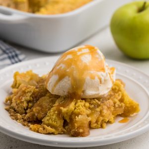 Dump cake with ice cream and caramel sauce on a white plate.
