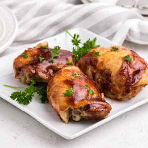 BBQ Chicken Thighs garnished with parsley and on a white plate.