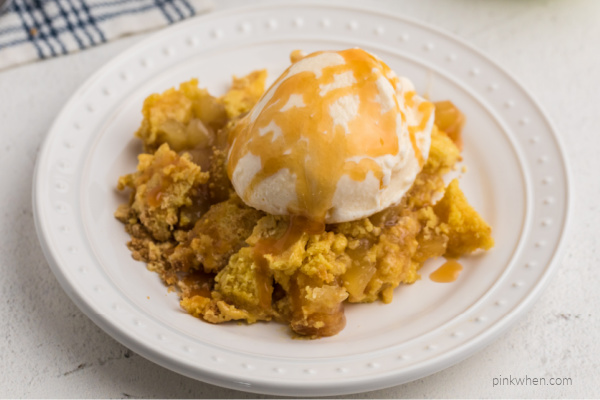 Apple Pie Filling Dump Cake with vanilla ice cream and caramel sauce on a white plate.