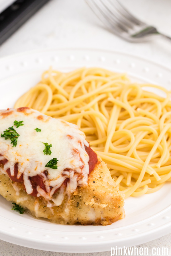Oven baked chicken parmesan with noodles on a white plate. 
