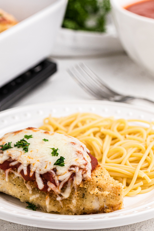oven baked chicken parmesan on a plate with noodles. 
