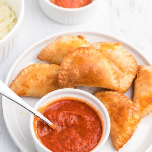 Homemade Air Fryer Pizza Rolls on a white plate with pizza dipping sauce.