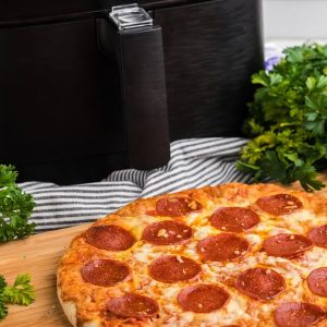 Pizza on a cutting board with a air fryer in the background.