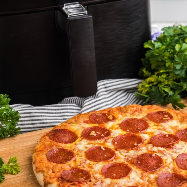 Pizza on a cutting board with a air fryer in the background.