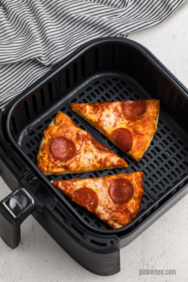 Slices of pizza in an air fryer basket. 