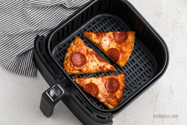 Slices of pizza in an air fryer basket. 