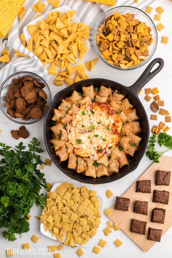 Skillet pizza rolls and pizza dip on a table full of snacks. 