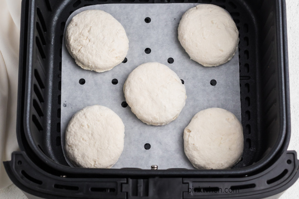 Biscuits placed on parchment paper in a single layer in an air fryer. 
