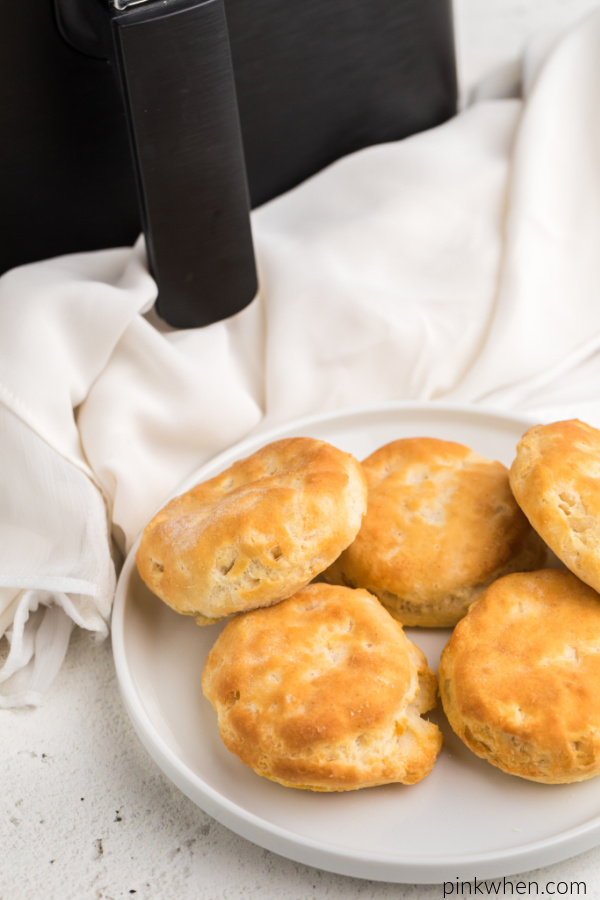 Biscuits on a white plate and an air fryer in the background. 