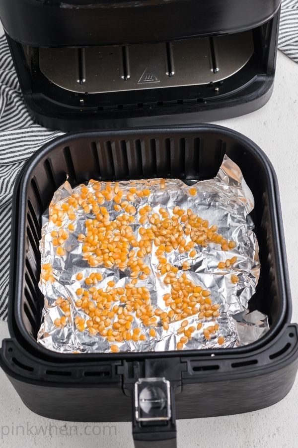 Air fryer basket with foil and corn kernels for popcorn