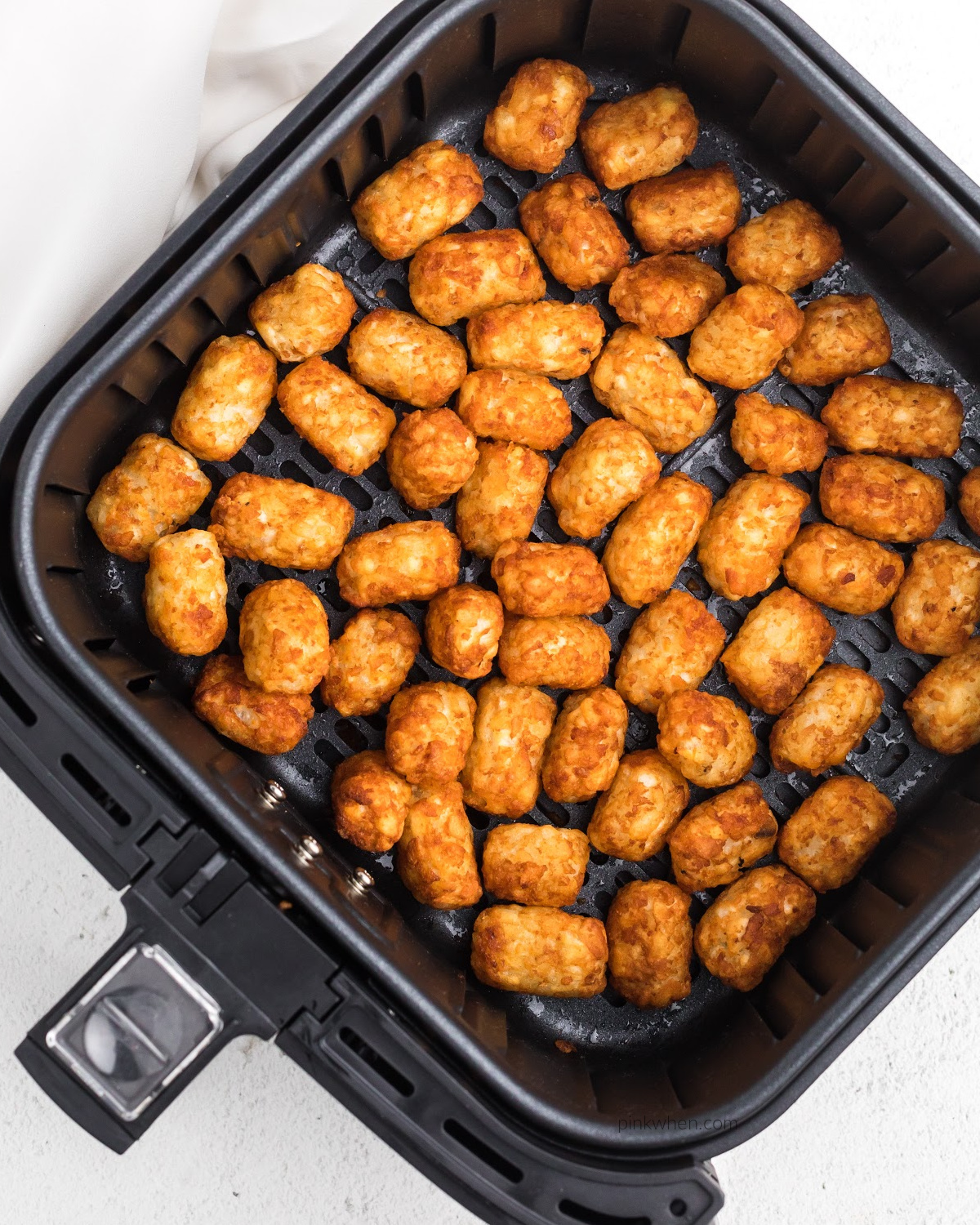 Crispy cooked frozen tater tots in air fryer basket. 