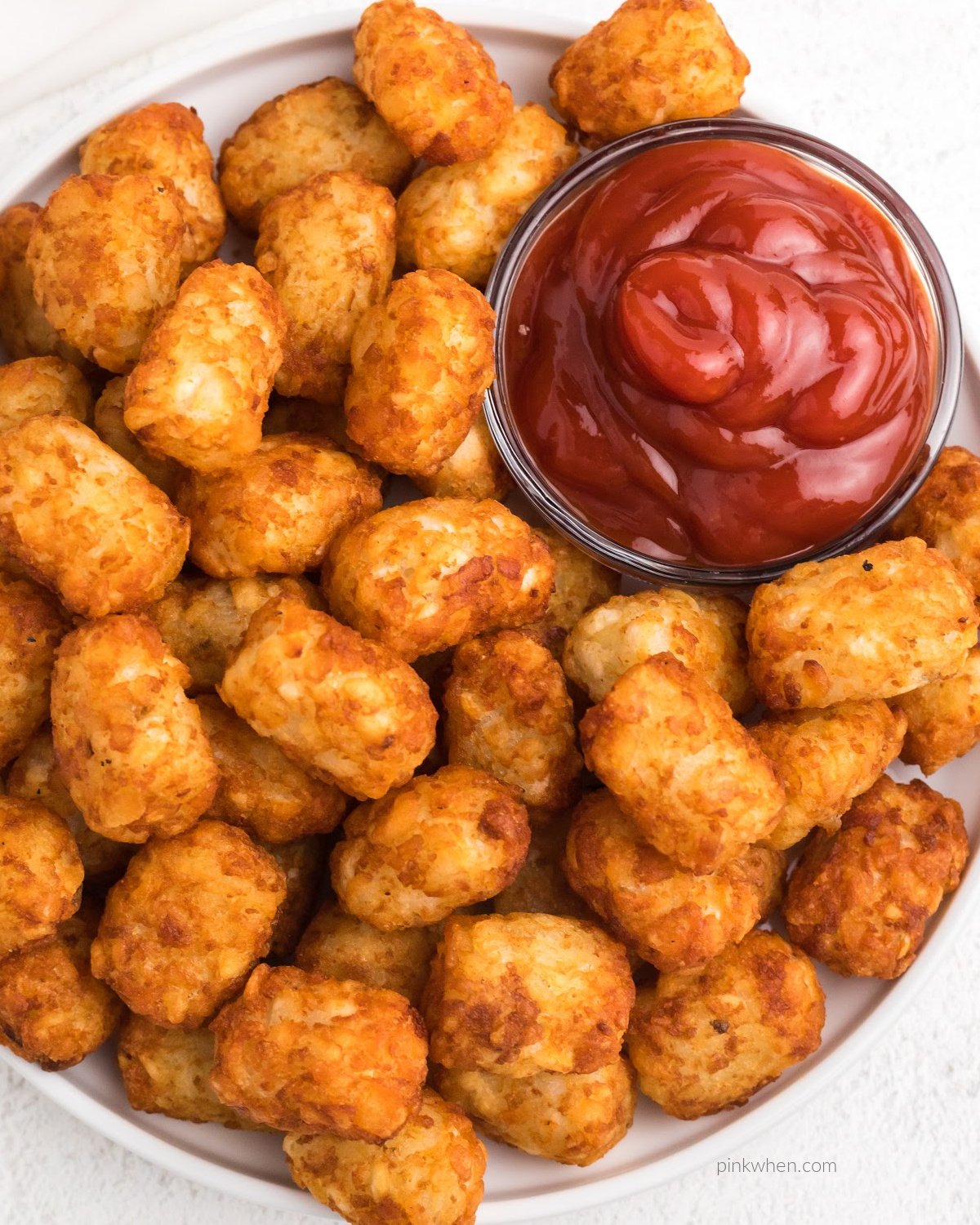 Tater tots on a white plate served with ketchup. 