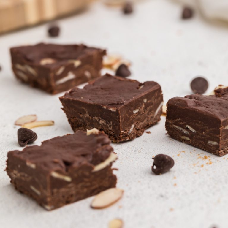 Chocolate fudge with almonds scattered on a white tabletop.