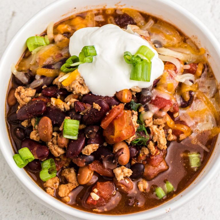 Pressure Cooker Turkey Chili in a white bowl and topped with sour cream and green onion tops.