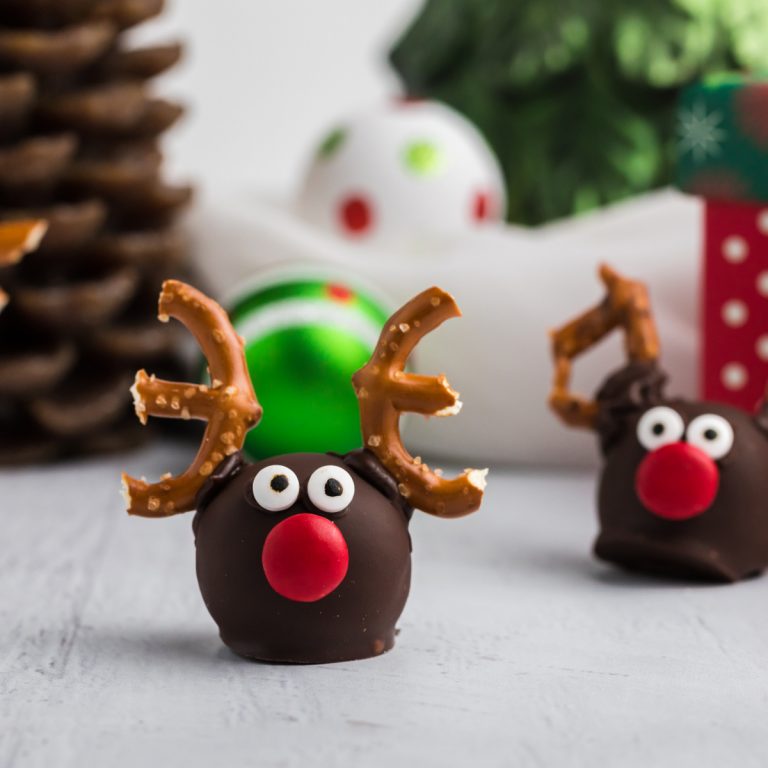 Truffles shaped like reindeeron a white table top with Christmas deocr in the background.