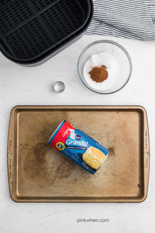 Grands biscuit dough on a cookie sheet and cinnamon and sugar in a bowl.