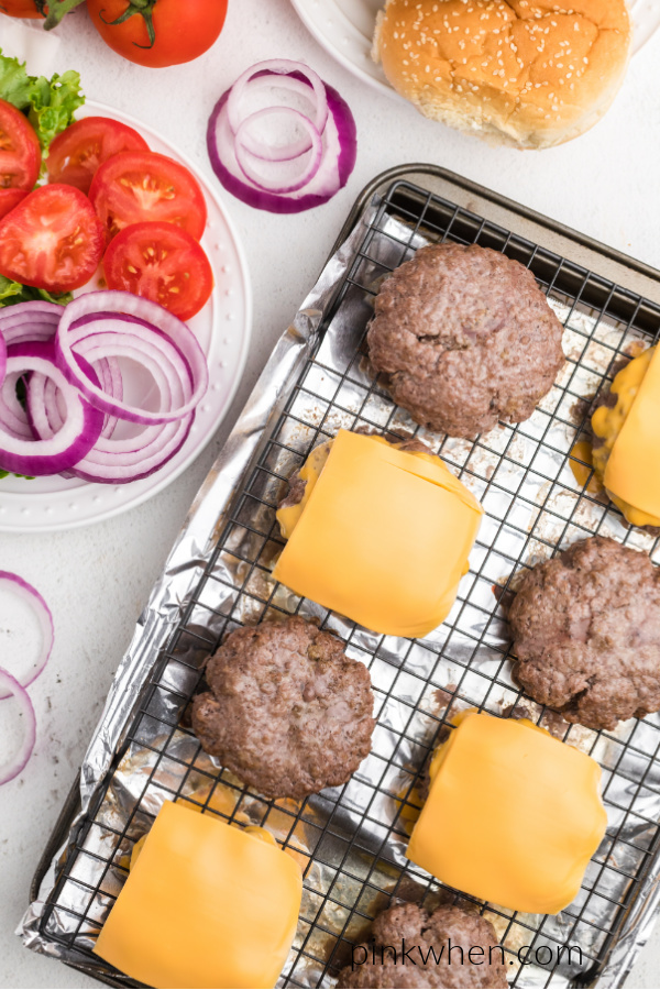 Oven baked hamburgers with cheese and plain burgers on a cooling rack over a cookie sheet. 