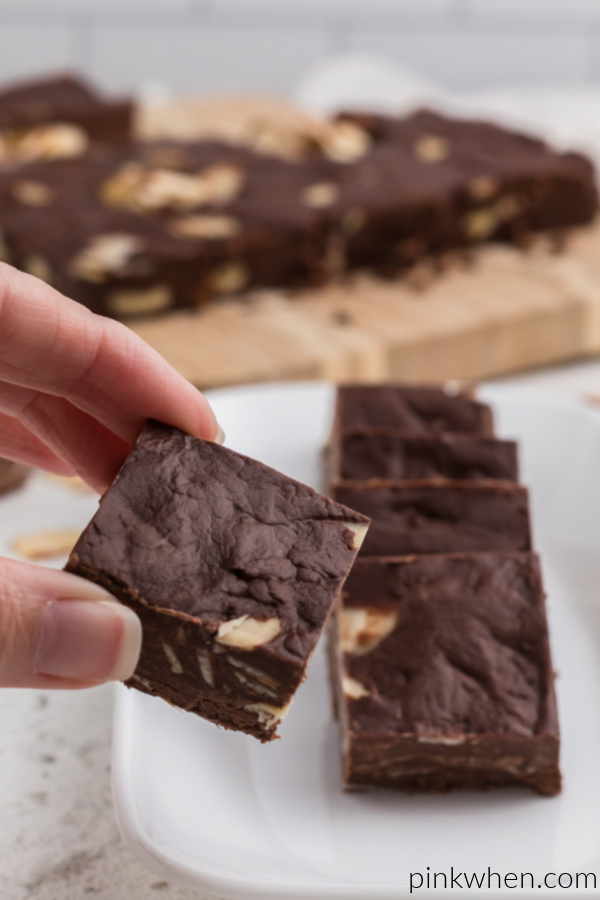 Chocolate fudge lined on a white platter with a hand holding a piece of fudge. 