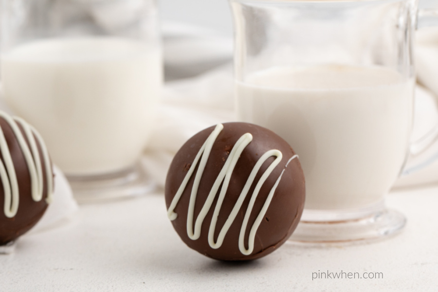 Hot chocolate bomb sitting in front of a glass of milk on a white table. 