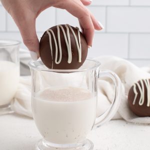 Hot chocolate bomb being placed into a clear glass of white milk