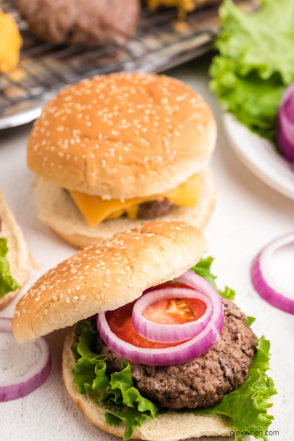 Fully cooked baked hamburger on a bun and dressed with lettuce, onions, and a slice of tomato.
