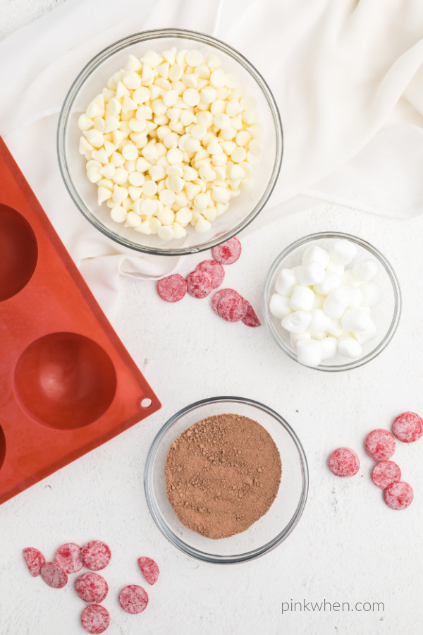 Ingredients on top of a white tabletop used to make hot chocolate bombs for Valentines day.