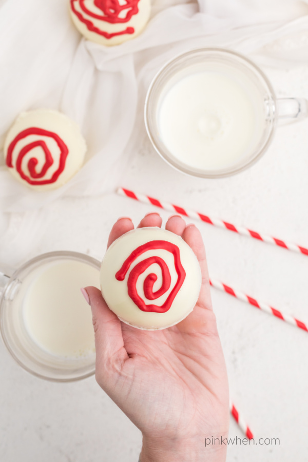 Hand holding a hot chocolate bomb made with white chocolate and decorate with red candy melts.