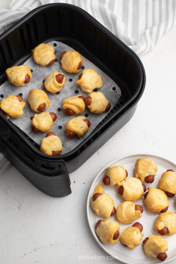 Pigs in a Blanket in the basket of an Air Fryer and on a white plate.