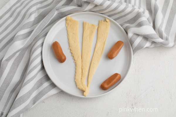 Crescent dough pastry sheet cut into thirds and cocktail sausages on a white plate.