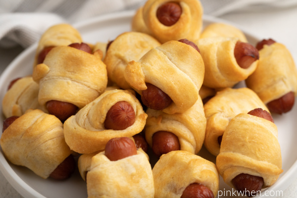 Cooked crescent dog sausages on a white plate.