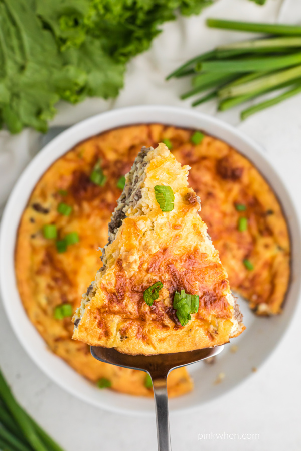 A slice of cheeseburger pie being held up over the full plate of cheeseburger pie.